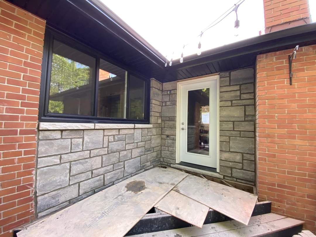 Grey stone veneer around a back door between two red-brick walls